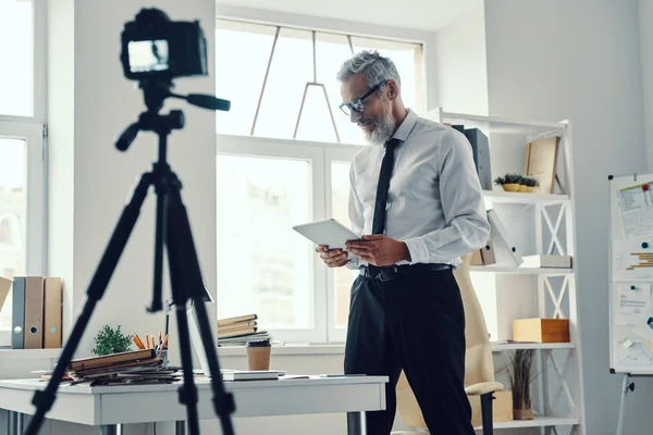 Впевнений зрілий чоловік в елегантній сорочці і краватці, використовуючи цифровий планшет, роблячи відео в соціальних мережах — стокове фото
