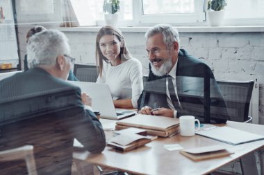 Başarılı iş adamları modern teknolojileri kullanarak satışları analiz ediyor ve yönetim kurulunda personel toplantısı yaparken gülümsüyor.     