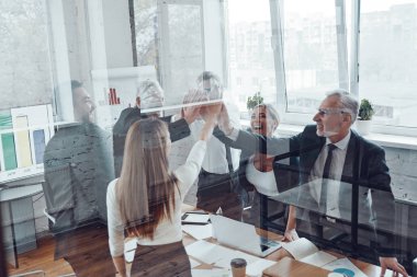 Neşeli iş adamları modern ofiste çalışırken birbirlerine beşlik çakıyorlar.