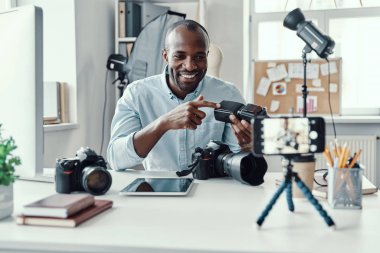 Çekici genç Afrikalı gömlekli adam dijital kamera gösteriyor ve sosyal medya videosu çekerken bir şeyler anlatıyor. 