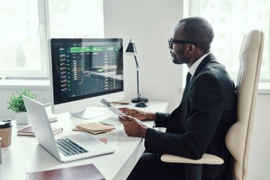 Ofiste çalışırken modern teknolojileri kullanan resmi giysili Afrikalı genç bir adam.