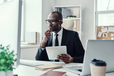 Ofiste çalışırken modern teknolojileri kullanan resmi giysili Afrikalı genç bir adam.    