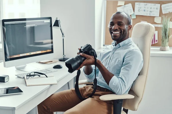 在现代办公室工作时 英俊的非洲年轻人拿着数码相机 面带微笑 — 图库照片