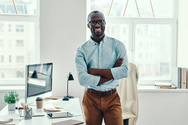 Happy young African man in shirt looking at camera and smiling while working in the office           