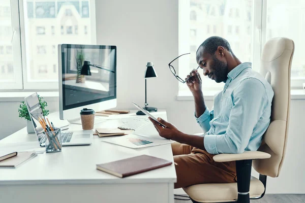 オフィスで働いている間 デジタルタブレットを使用してシャツの中に集中した若いアフリカ人男性 — ストック写真