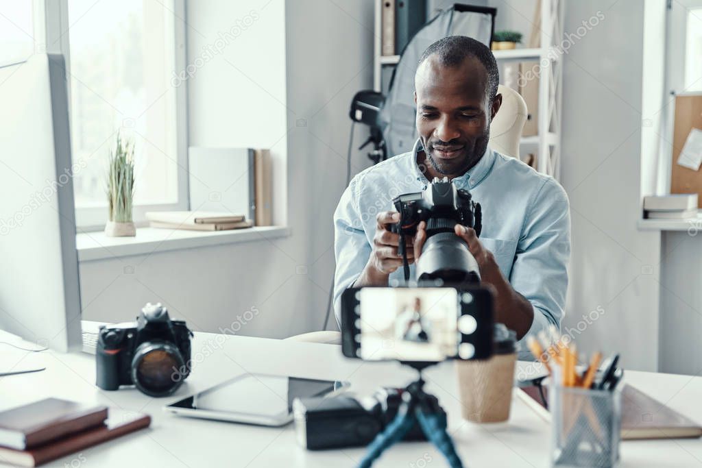 Handsome young African man in shirt showing digital camera while making social media video