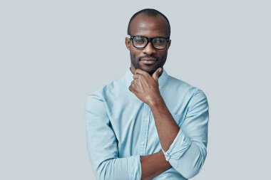 Çekici Afrikalı genç bir adam gri arka planda kameraya bakıyor.               