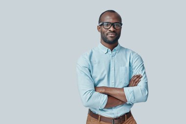 Gri arka planda dururken kameraya bakan kendinden emin genç Afrikalı adam     