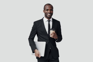 Resmi giyinmiş genç Afrikalı adam gri arka planda dururken kameraya bakıp gülümsüyor.