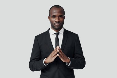 Resmi giyinmiş yakışıklı Afrikalı genç adam gri arka planda dururken kameraya bakıyor.   
