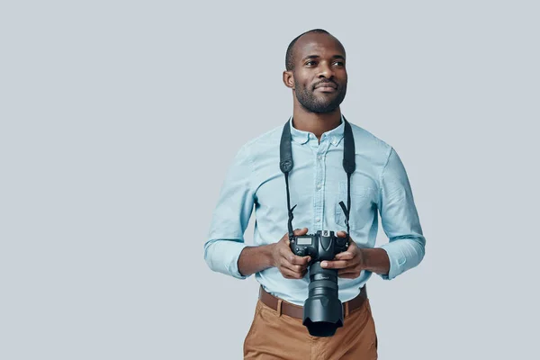 ハンサムな若いですアフリカ人男性とともにデジタルカメラ見ながら離れて立っている間灰色の背景 — ストック写真