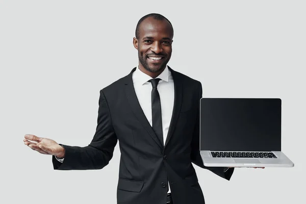 穿着正式衣服的现代非洲年轻人 一边站在灰色的背景下 一边在笔记本电脑上指着复制的空间 微笑着 — 图库照片