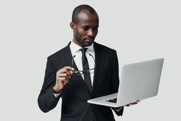 站在灰色背景下 穿着正装 用电脑工作的专注的非洲年轻人 — 图库照片
