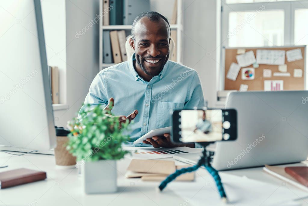 Handsome young African man in shirt telling something and smiling while making social media video