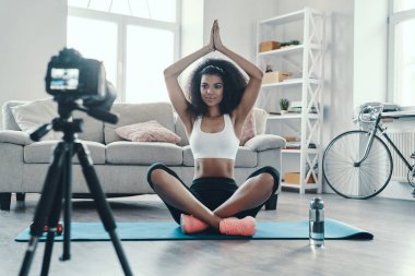 Sosyal medya videosu çekerken yogada oturan güzel bir Afrikalı kadın.                  