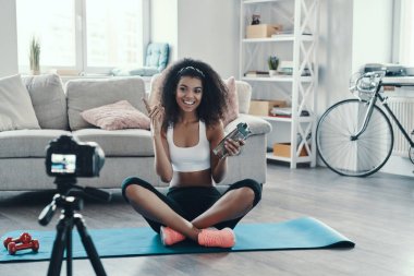 Genç Afrikalı kadın sosyal medya videosu çekerken spor yapıyor ve gülümsüyor.
