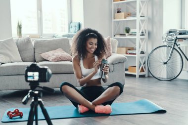 Çekici genç Afrikalı kadın sosyal medya videosu yaparken spor yapıyor ve gülümsüyor.
