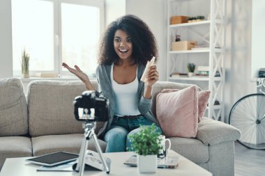 Sosyal medya videosu çekerken elinde güzellik ürünü tutan ve gülümseyen mutlu genç Afrikalı kadın.          