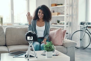 Sosyal medya videosu çekerken kendine güvenen genç Afrikalı kadın bir şeyler anlatıyor ve gülümsüyor.         