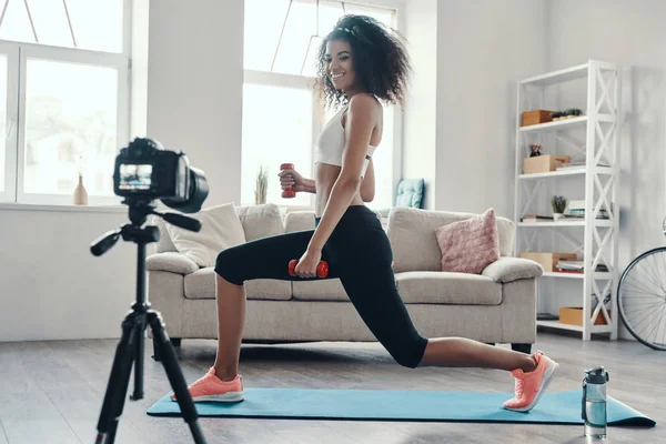 Attractive young African woman exercising using hand weight and smiling while making social media video