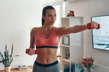 Spor elbiseli genç bir kadını kazanmaya karar verdim. Oturma odasında çalışırken dambılla yumruk atmaya. 
