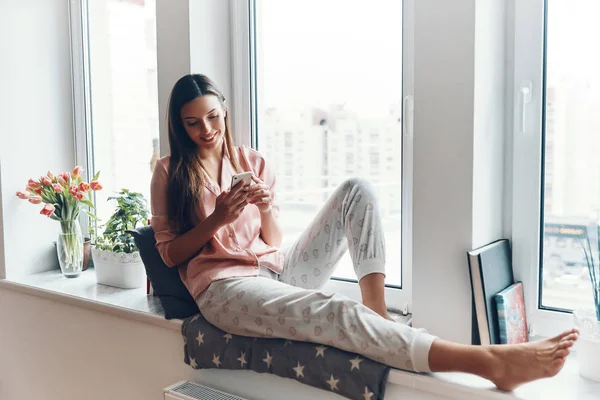 Femeie Tânără Frumoasă Pijamale Confortabile Folosind Smartphone Zâmbind Timp Odihnește — Fotografie, imagine de stoc