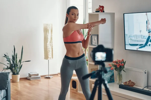 Attractive young woman in sports clothing working out and smiling while making social media video