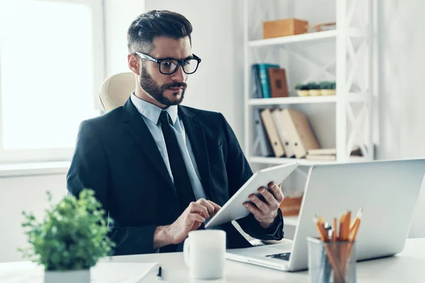 オフィスに座っている間 デジタルタブレットを使用して作業エレガントなビジネススーツの集中若い男 — ストック写真