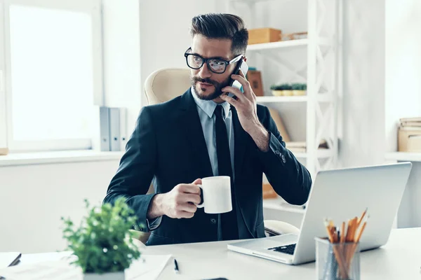 Şık Takım Elbiseli Gülümseyen Genç Adam Ofiste Otururken Akıllı Telefondan — Stok fotoğraf