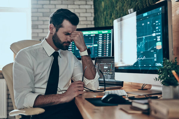 Разочарованный молодой человек в формальной одежде массирует нос, сидя в офисе
