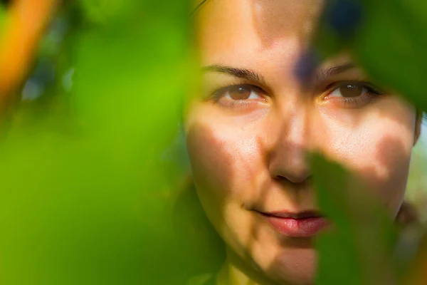 葉と太陽の光に照らされながら 若い女性の選択的焦点を当てた肖像画 — ストック写真