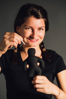 Siyah arka planda izole edilmiş siyah bir tekstil voodoo bebeğiyle oynayan gülümseyen genç bir kadın.