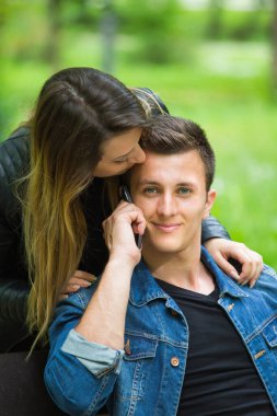 Kız arkadaşı onu alnından öperken telefonda konuşan gülümseyen bir adamın yakın çekimi. 