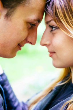 Birbirlerinin gözlerine bakıp gülümseyen genç aşıkların portresi. 