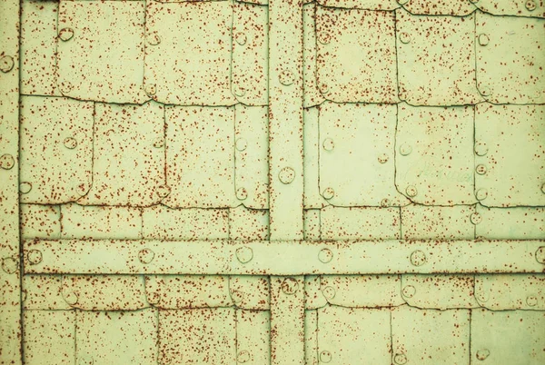 Perçin ve kaburgalar, kahverengi pas lekeleri kare sayfalardan gelen sarı-yeşil demir kapı