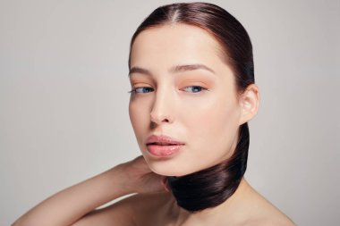 Mavi gözlü, dolgun dudaklı, genç ve güzel bir kız saçlarını tutuyor. Gri arka plan. Koyu renk. Aşağıya bakıyorum. Boşluğu kopyala.