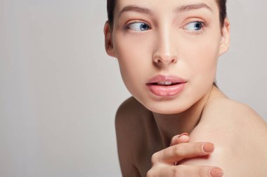 Çerçeveyi kapatın. Güzel bir kız sol elini omzunda tutuyor ve arka plana bakıyor. Boşluğu kopyalayın.