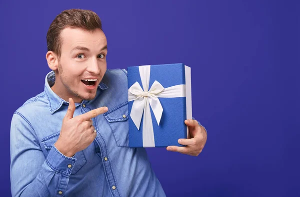 Joyful happy young man in a blue denim shirt shows the index finger on gift — 图库照片