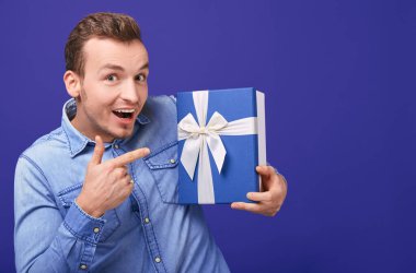 Joyful happy young man in a blue denim shirt shows the index finger on gift