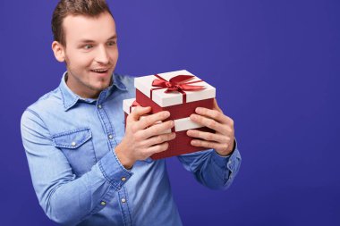 Surprised man in blue denim shirt standing with two gifts with a red cap