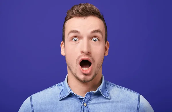 Surprised young man in a blue denim shirt standing with two standing with his mouth open — Stockfoto