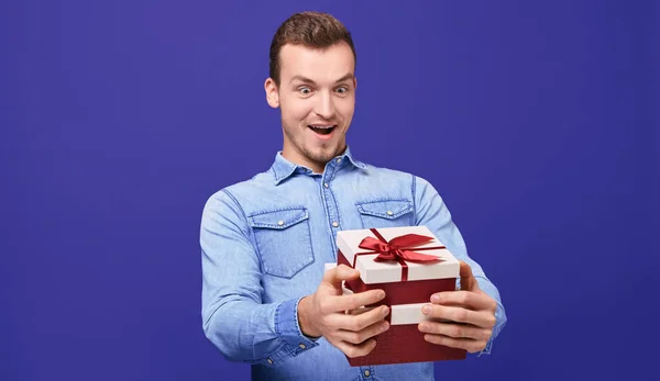 Surprised guy in blue denim shirt and round glasses with two gifts in his hands — 图库照片