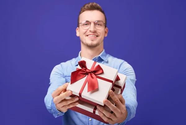 Cheerful guy in blue denim shirt and round glasses giving you gift — 图库照片