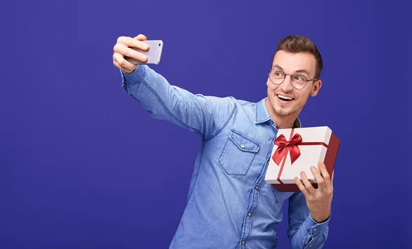 Young guy with present in his hand making selfie. — 图库照片