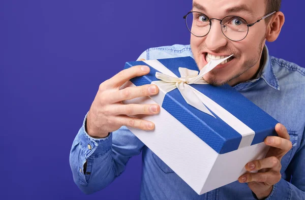 身穿蓝色斜纹棉布衬衫和眼镜的男子试图解开带着牙齿的礼物 — 图库照片