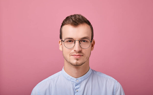 young man in a sky blue shirt and computer glasses posing on pink background 