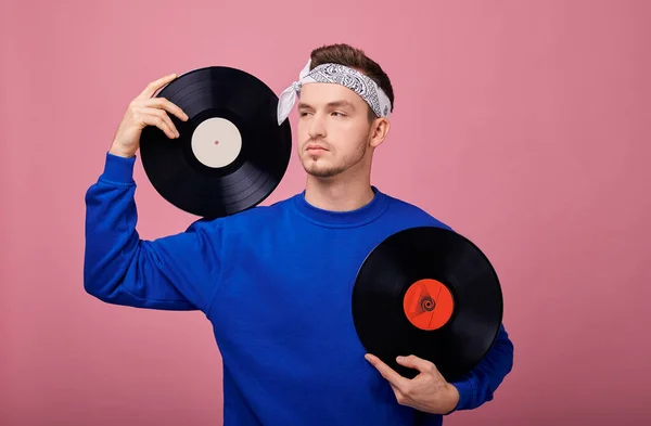 Närbild. En cool kille i en bandana i mörkblå jacka står på en rosa bakgrund med en svart vinylskiva i handen. Ungdom, stil, självförtroende, glädje, lekfullt humör. Leende. — Stockfoto