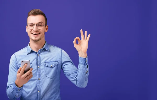 Kot gömlekli genç adam elinde cep telefonu tutuyor ve iyi görünüyor.