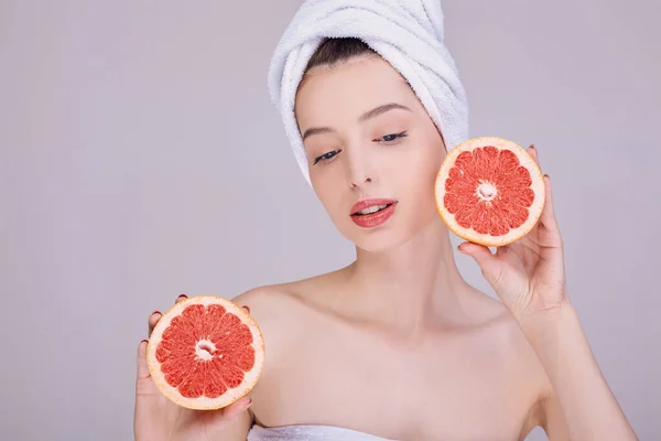 Menina com a pele limpa, semi-nua, em uma toalha na cabeça, segura em suas mãos uma toranja fresca . — Fotografia de Stock