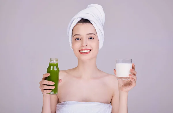 Smiling girl in a towel holds a glass of milk and a bottle with smoothie. — Stock Photo, Image